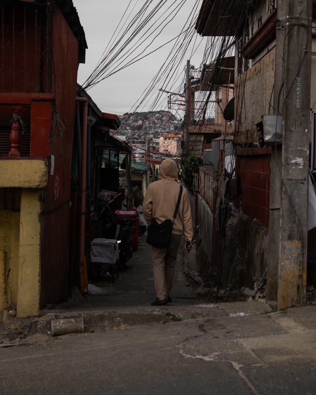 A man wearing a hooded brown jacket entering an alley